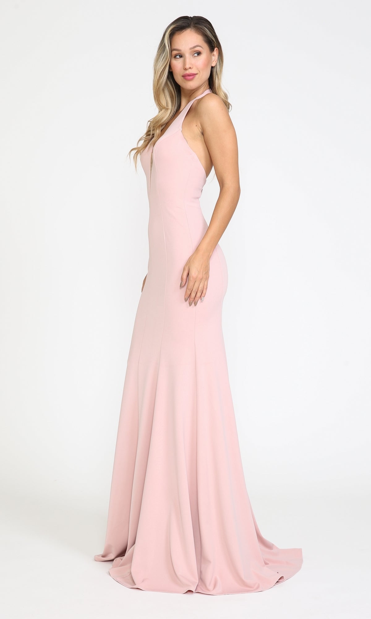 A woman models the Halter V-Neck Long Jersey Formal Prom Dress 8262, a sleeveless, light pink floor-length gown, posing against a plain white background with one hand by her side.